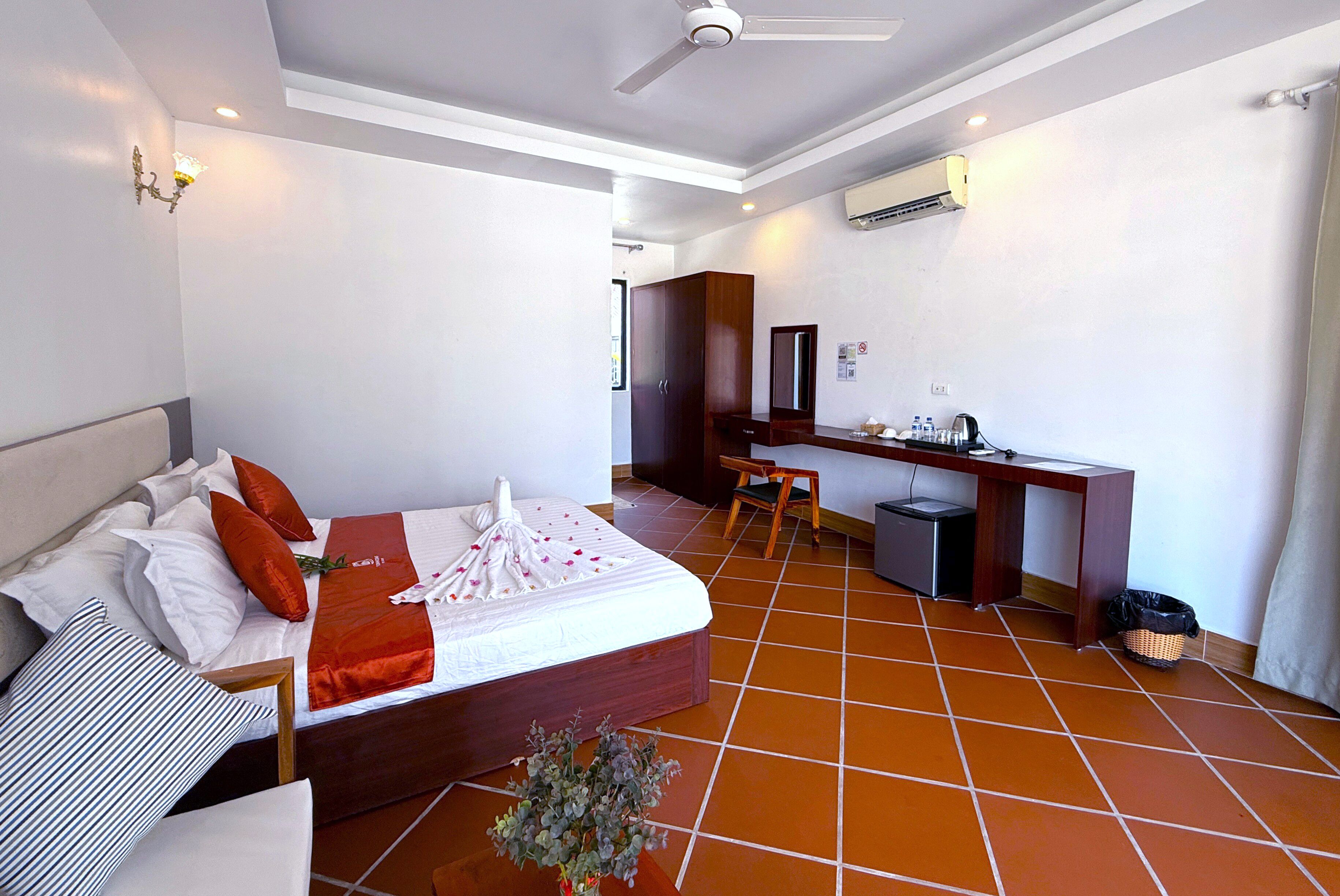 A hotel room with a bed, desk, chair, and a small trash bin.