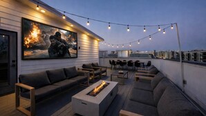 Eine Dachterrasse mit Feuerstelle, Sitzgelegenheiten im Freien, Lichterketten und einem großen Gemälde.