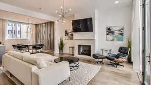 Ein geräumiges Wohnzimmer mit einem modernen Sofa, einem Essbereich, einem Kamin und einem großen Wandfernseher.