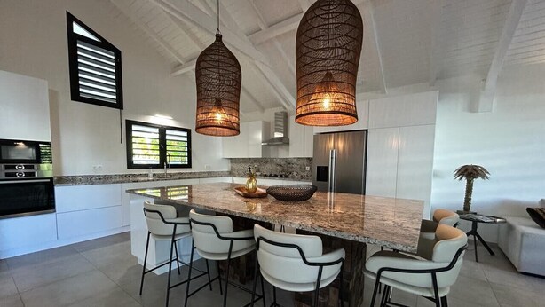 A modern kitchen with a large island, bar stools, pendant lights, and a view of the outdoors.