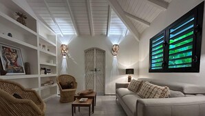 A modern living room with a high ceiling, white walls, and a large window with green blinds.