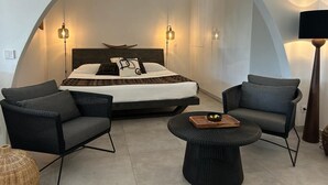 A bedroom with a bed, two chairs, a small table, and a lamp.