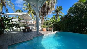 A pool area with a wooden deck, potted plants, and a white gazebo structure.