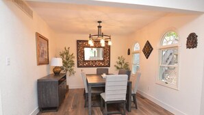 A dining area with a wooden table, chairs, a chandelier, and a mirror on the wall.