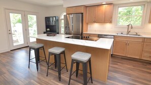 A modern kitchen with a large island, stainless steel appliances, wooden cabinets, and a window providing natural light.