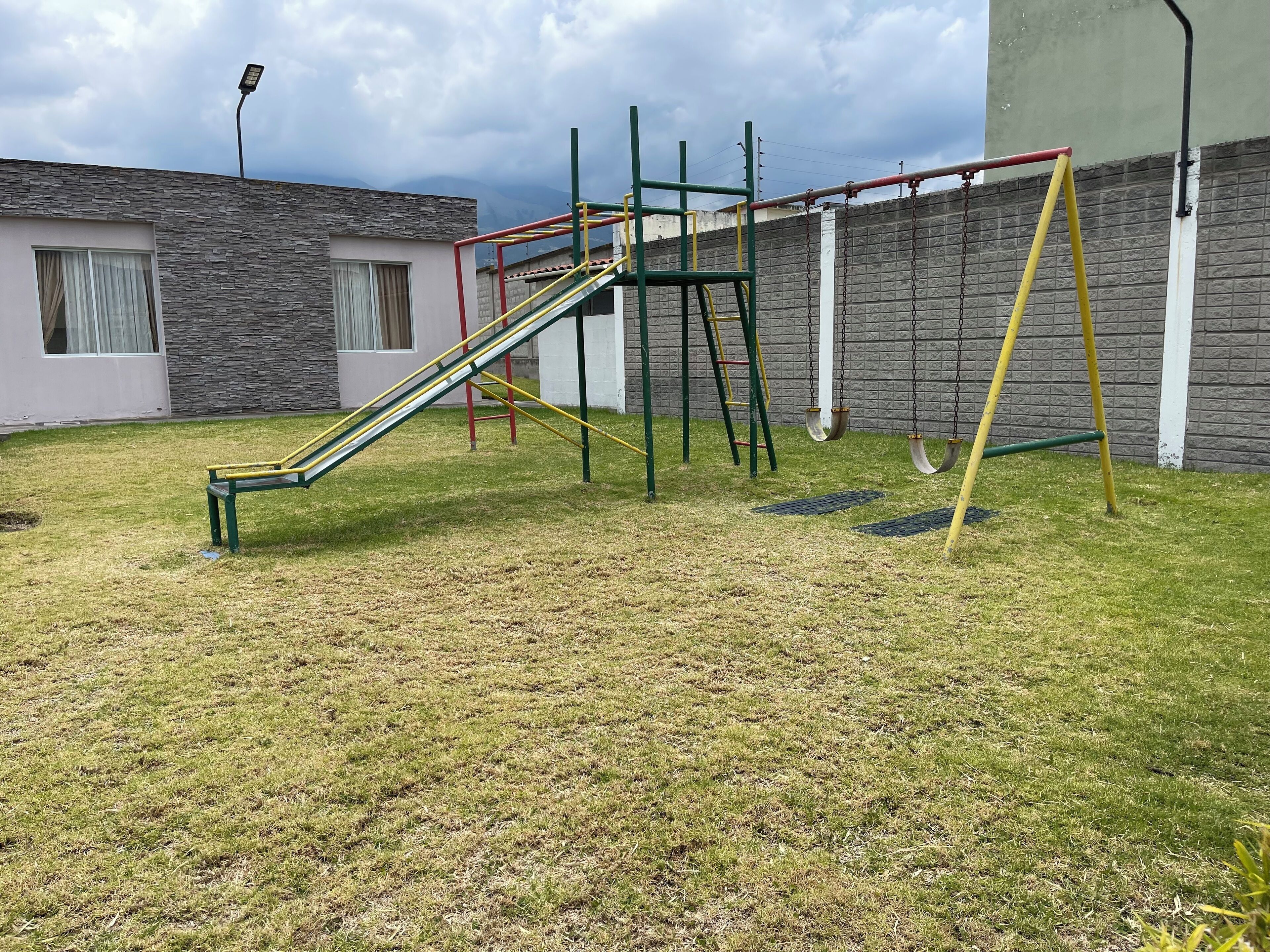 Un parque infantil con tobogán, estructura de escalada y columpios.