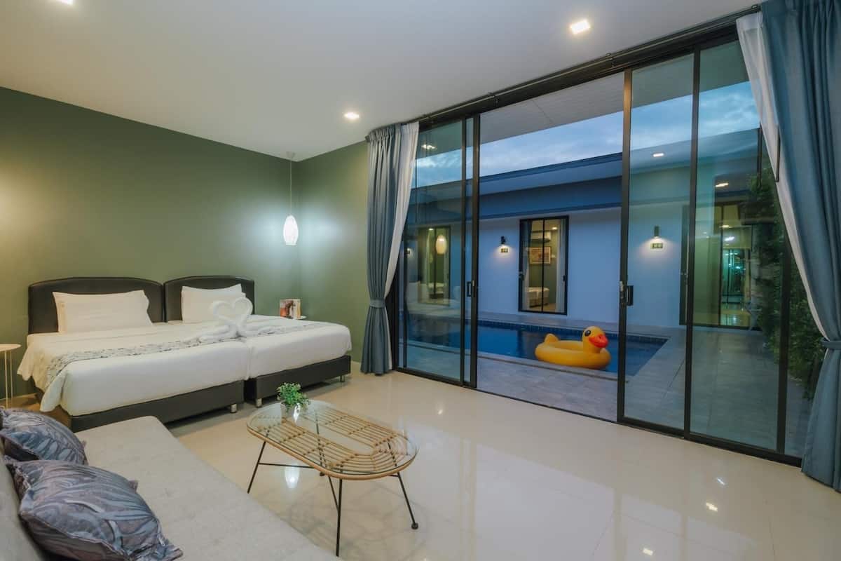 A modern bedroom with a large bed, a glass door leading to a pool area, and a small table with a plant.