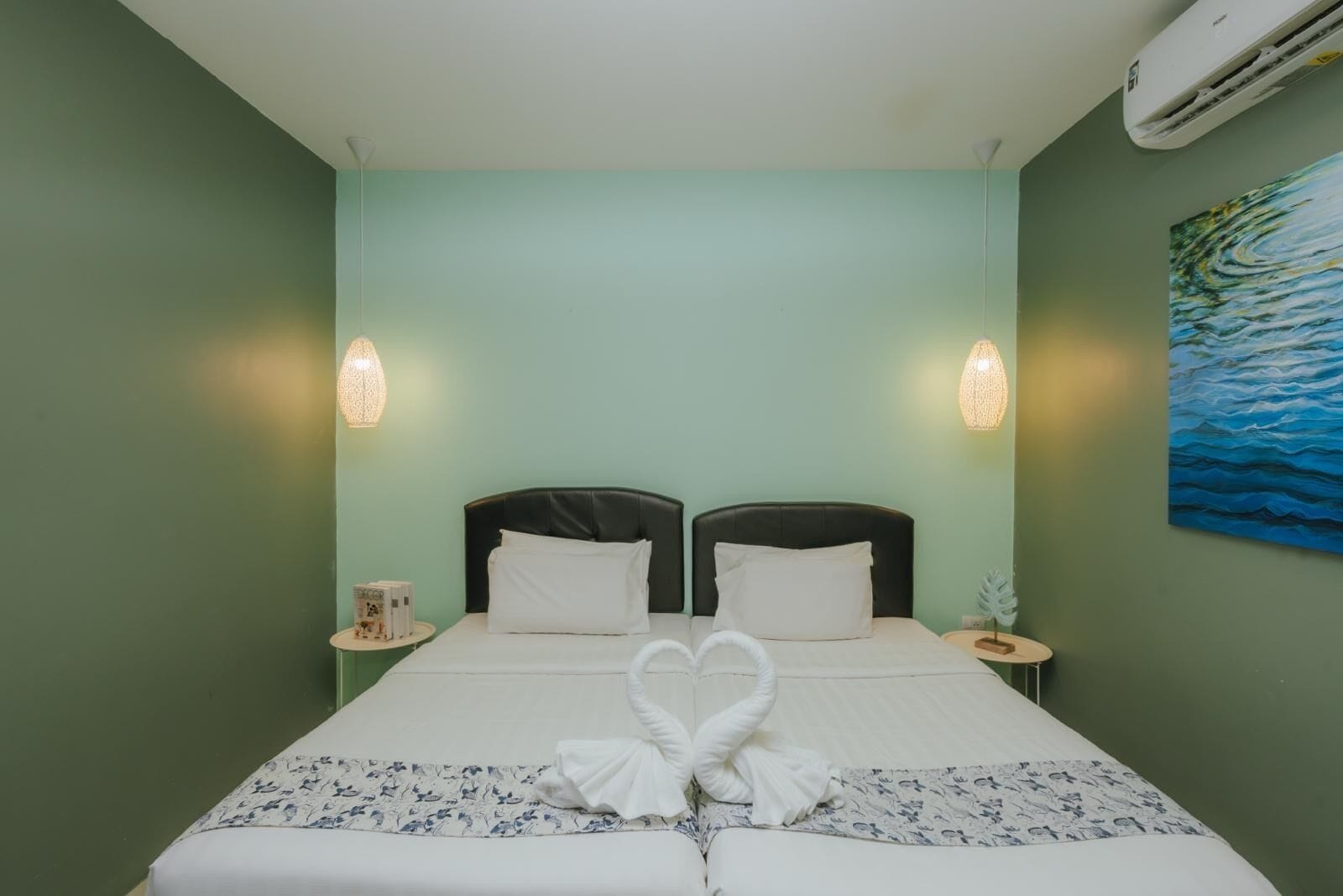 A hotel room with two beds, a painting on the wall, and a towel art on the bed.