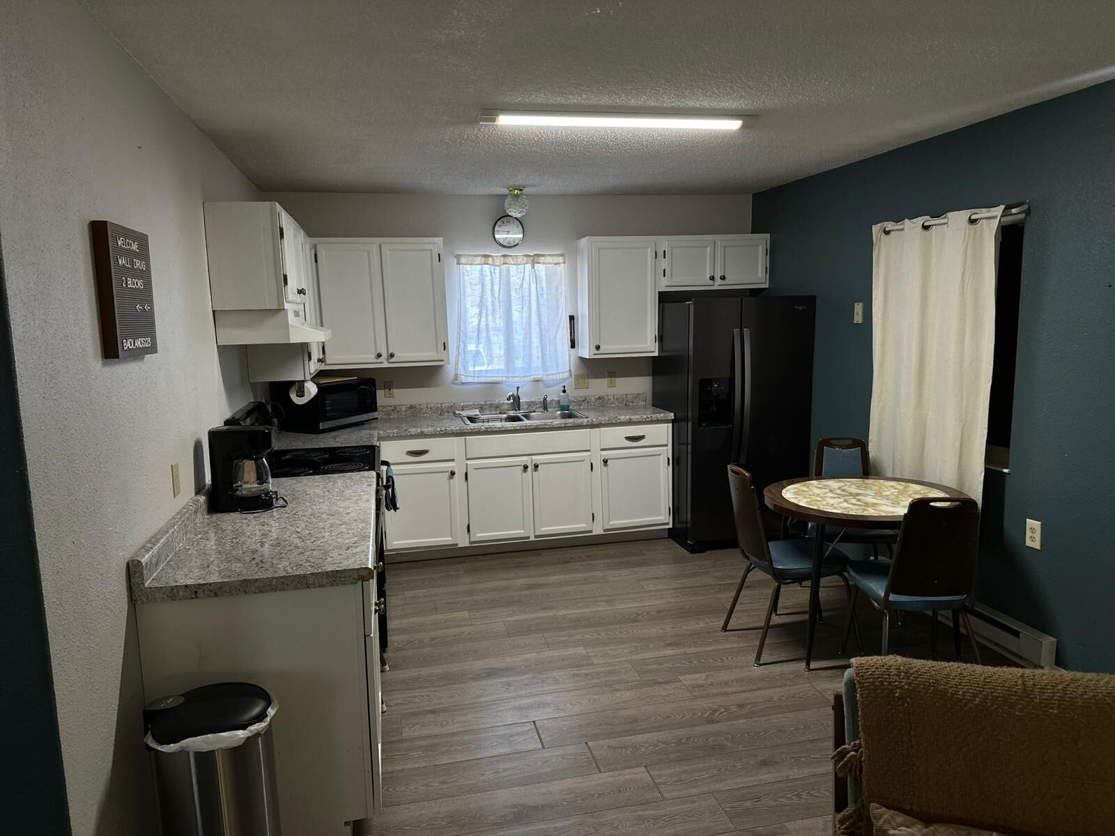 A compact kitchen with white cabinets, a refrigerator, a coffee maker, and a dining area with two chairs.