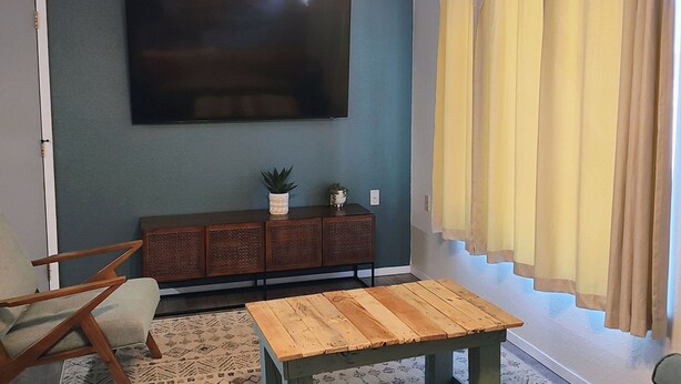 Un salon doté d’un ventilateur de plafond, d’un téléviseur à écran plat fixé au mur, d’un banc en bois, d’une table basse et d’un canapé avec des coussins.