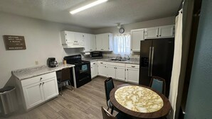 Une cuisine compacte avec des meubles blancs, une cuisinière noire, un réfrigérateur et une table à manger en marbre.