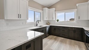 A modern kitchen with white cabinets, a marble countertop, and a view of the outdoors through large windows.