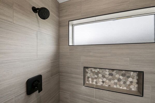 A shower area with a rain showerhead, a window, and a decorative stone panel.