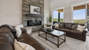 A modern living room with a stone fireplace, leather sofas, and large windows offering a view of the countryside.