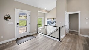 A spacious hallway with a wooden floor, a glass door leading outside, and a black railing.