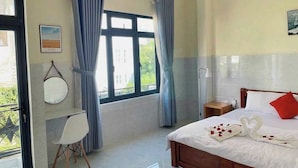 Habitación de hotel con cama, escritorio, silla, ventana con cortinas y vista a zonas verdes.