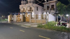 Una casa de dos pisos con un acceso mediante portón, una motocicleta estacionada afuera y un cielo nocturno despejado.