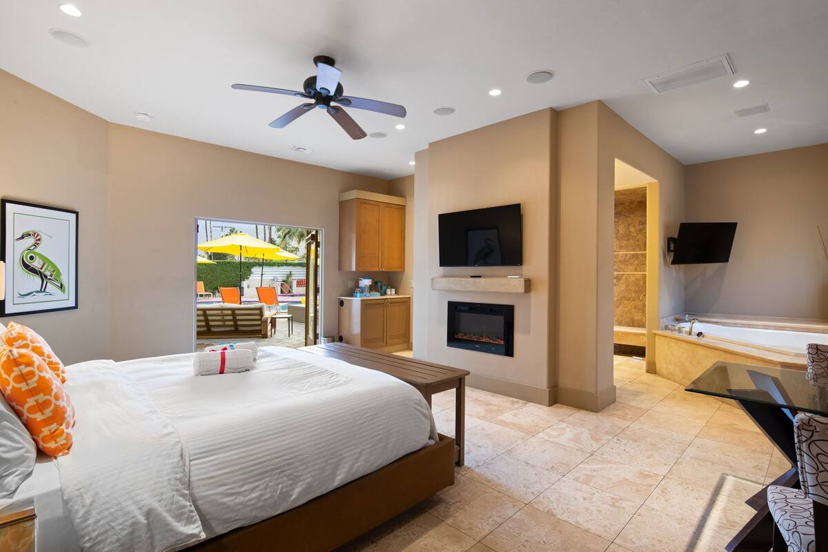 A hotel room with a bed, a ceiling fan, a fireplace, a TV mounted on the wall, and a bathroom with a bathtub and shower.
