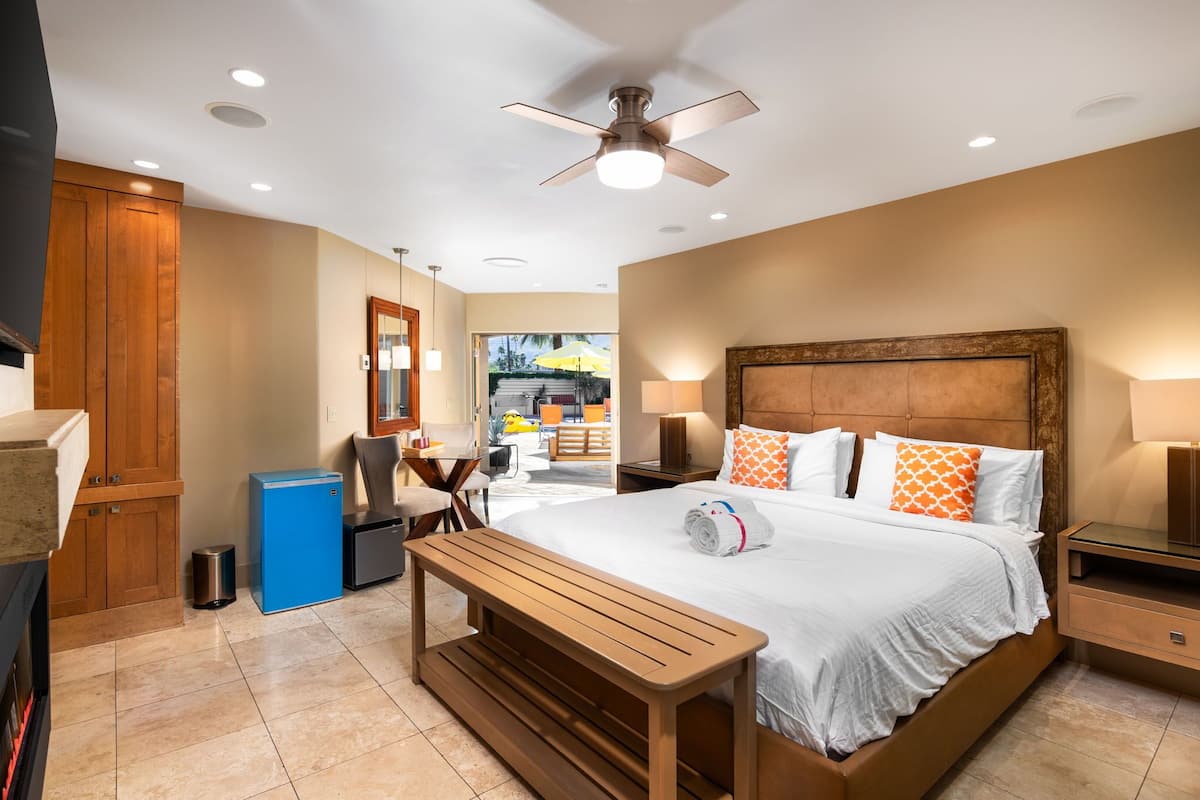 A modern hotel room with a large bed, wooden headboard, bedside tables, a desk, and a bench.