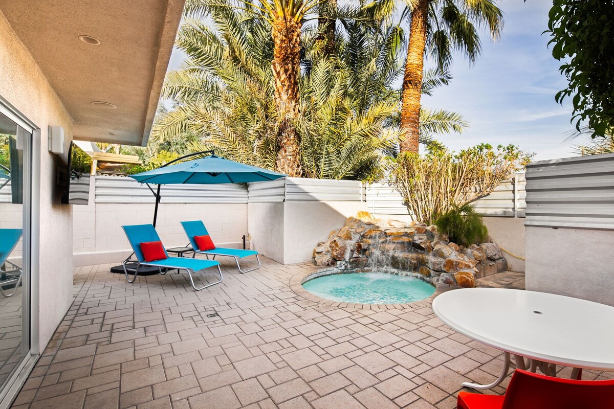 A patio with a pool, lounge chairs, and a table.