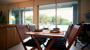A dining area with a table set for four, large windows, and a view of greenery outside. - Apartment FALCÓN by HR COSTABRAVA (Castell-Platja d'Aro)