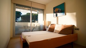 A bedroom with a bed, a table, a chair, a lamp, and a painting on the wall. - Apartment FALCÓN by HR COSTABRAVA (Castell-Platja d'Aro)