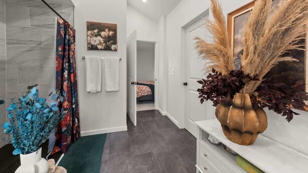 A modern bathroom with a shower, a toilet, and a sink. There is a towel rack on the wall and a decorative vase with dried plants.