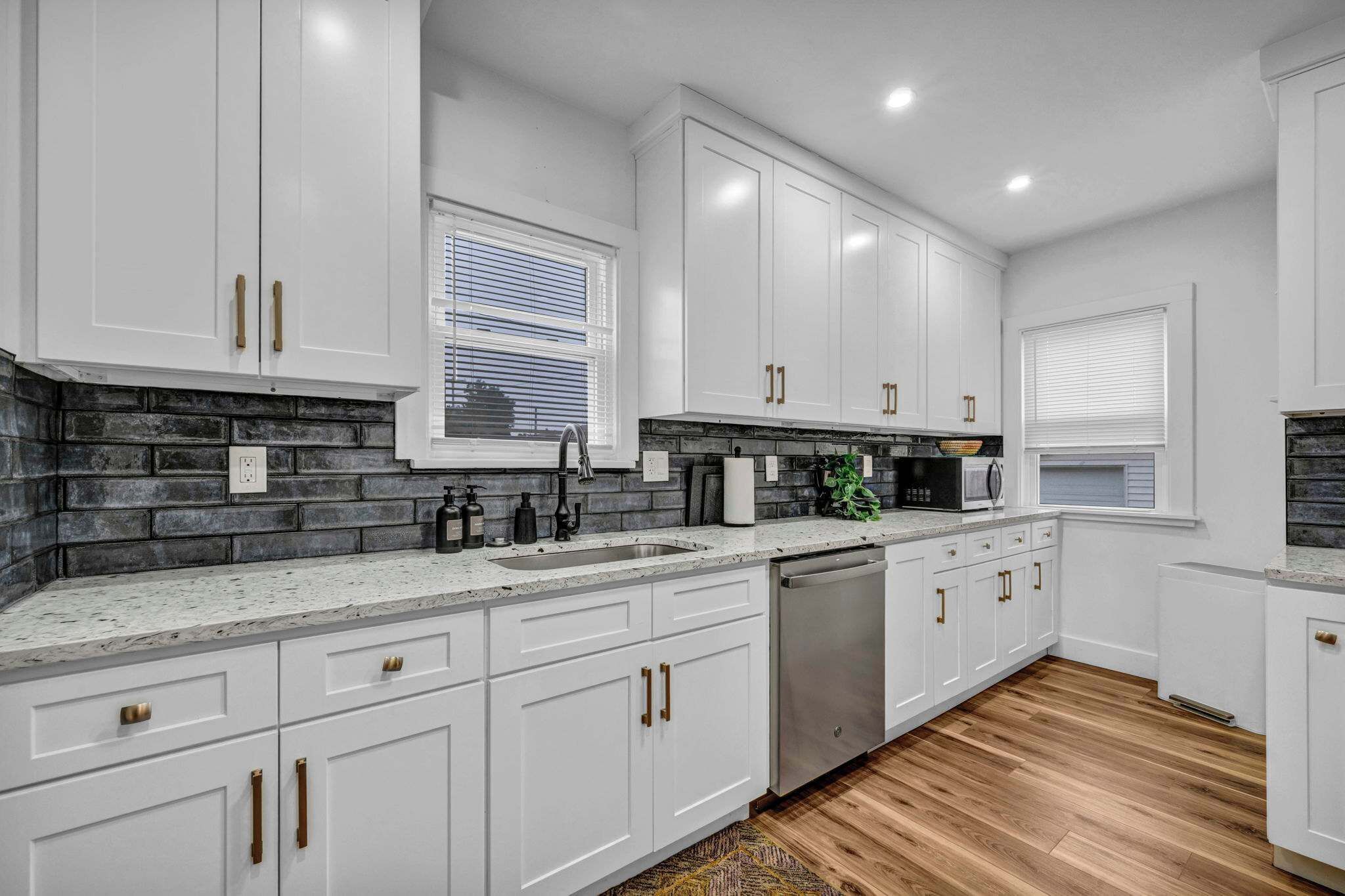 A modern kitchen with white cabinets, a stainless steel dishwasher, and a granite countertop.