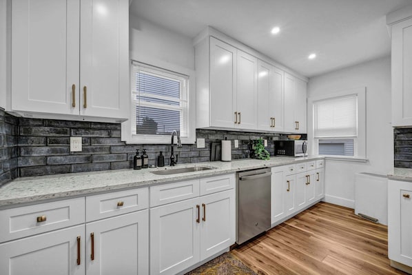 A modern kitchen with white cabinets, a stainless steel dishwasher, and a granite countertop.