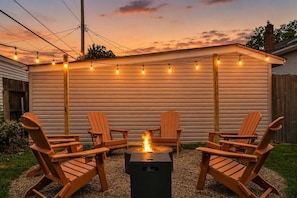 An outdoor seating area with wooden chairs and a fire pit, surrounded by a string of lights and a wooden fence. - Hot Tub - Game Room - FirePit - Minutes to Downtown Cleveland (Cleveland)