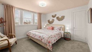 A bedroom with a bed, a chair, a bedside table, and a window with curtains.