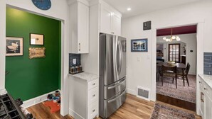 A modern kitchen with white cabinets, a stainless steel refrigerator, and a green accent wall.
