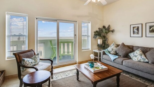 A living room with a sofa, coffee table, and chairs. There is a sliding glass door leading to a balcony. - Pelicondo | Ocean Front Condo with Beach View (Galveston)