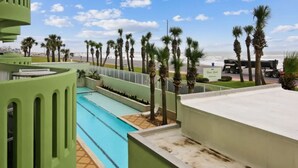 A swimming pool with a view of the beach and palm trees. - Pelicondo | Ocean Front Condo with Beach View (Galveston)
