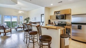 A spacious living area with a kitchen, including a dining set and a large refrigerator. - Pelicondo | Ocean Front Condo with Beach View (Galveston)