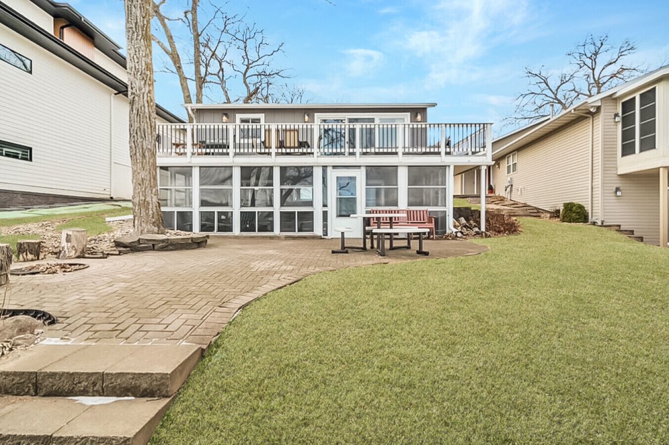 A two-story house with a balcony, a patio with a bench, and a well-maintained lawn.