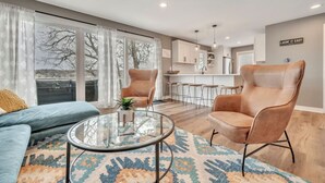 A modern living room with a sofa, two armchairs, a glass coffee table, and a patterned rug.