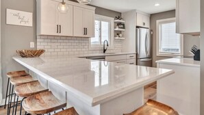 A modern kitchen with a large island, white cabinetry, and pendant lighting.