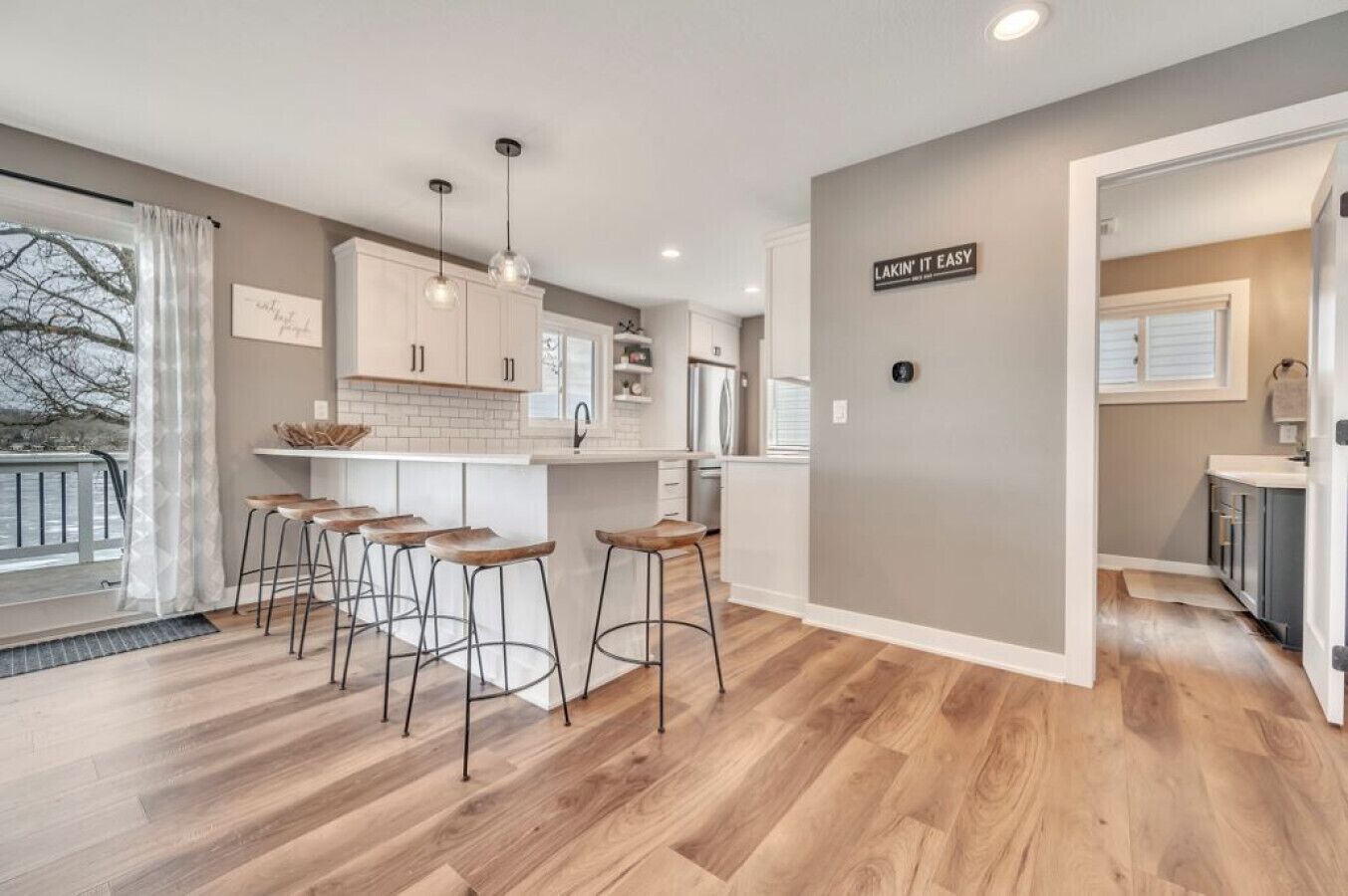 A modern kitchen with white cabinets, a central island with stools, and a sign on the wall.