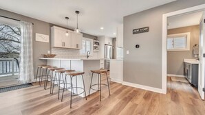 A modern kitchen with white cabinets, a central island with stools, and a sign on the wall.