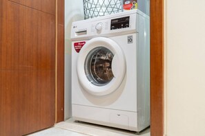 A front-loading washing machine in a laundry room with a wooden door and tiled floor. - Sophisticated and Elegant 2BR in Downntown Dubai (Dubai)