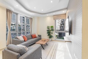 A modern living room with a grey sofa, a wooden coffee table, and a large window with a view of buildings.