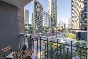 A balcony with a view of modern high-rise buildings, a road with vehicles, and a small garden area. - Sophisticated and Elegant 2BR in Downntown Dubai (Dubai)