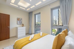 Habitación de hotel moderna con una cama grande, un tocador blanco, un cuadro y vistas a la ciudad a través de amplias ventanas.