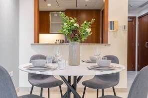 Un comedor con una mesa redonda dispuesta para dos personas, rodeado de sillas grises. En el centro, un jarrón con follaje verde y bayas rojas.