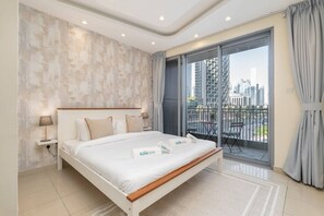 Un dormitorio moderno con una cama grande, una mesita de noche, una lámpara, una ventana con vistas a la ciudad y un balcón con una silla.
