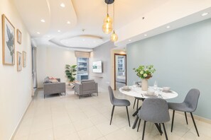A modern living room with a dining area, grey sofas, a round dining table set for four, and a large window with a view.