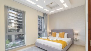 Une chambre à coucher moderne avec une grande fenêtre, un lit recouvert d’une couvre-lit grise et jaune, et un tapis à motifs.
