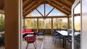 Una terrazza coperta all'aperto con tetto in legno, un tavolo da pranzo, sedie e un divano rosso.