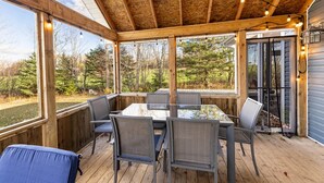 Una terrazza esterna coperta con tavolo e sedie in vetro, circondata da pareti in legno e ampie finestre.